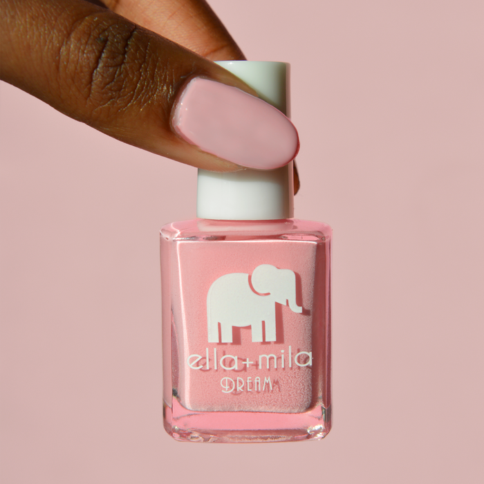 Get to the Pointe warm pink nail polish on a deep skin tone, holding the bottle on a pink background