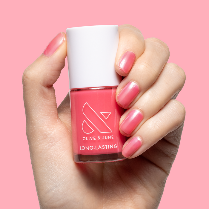 Hand with medium-length nails polished in sheer neon pink using Guava Gloss long-lasting nail polish on pink background