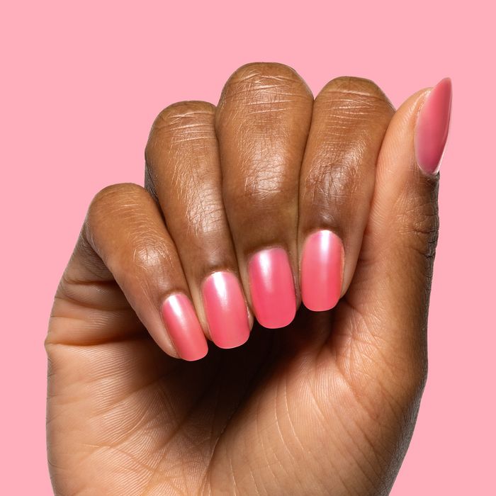 Hand with medium-length nails painted in sheer neon pink using Guava Gloss nail polish on pink background