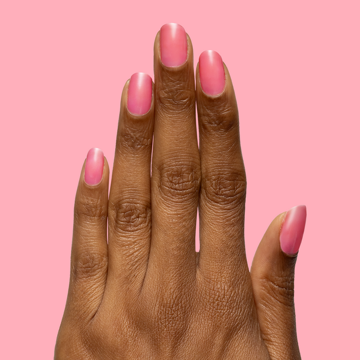 Hand with natural-length nails painted in sheer neon pink using Guava Gloss nail polish on solid pink background