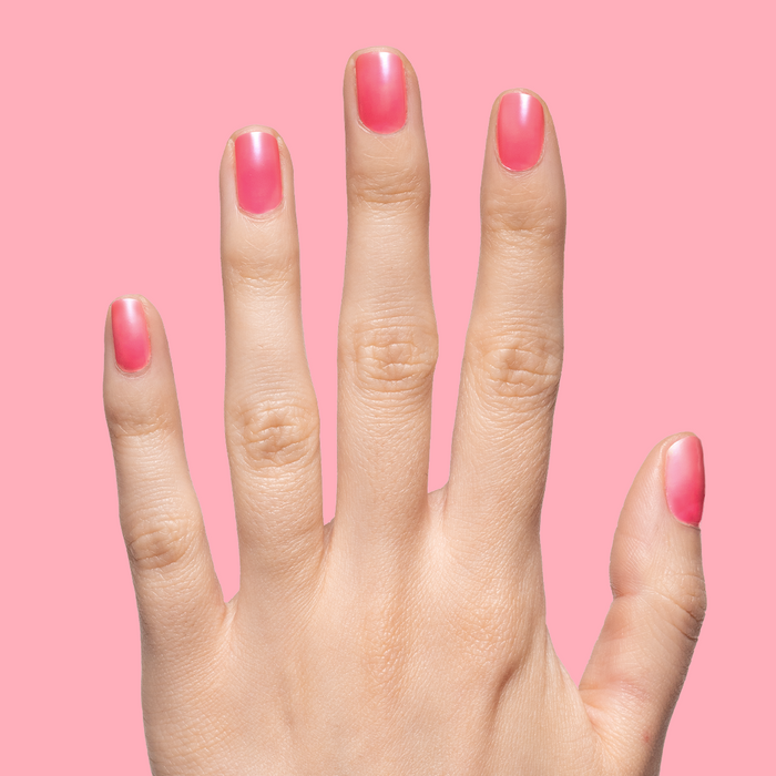 Hand with short natural nails coated in sheer neon pink Guava Gloss polish against solid pink background