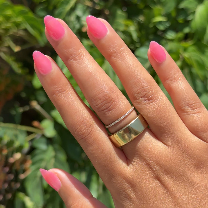 Hand with medium-length nails painted in sheer neon pink Guava Gloss polish outdoors with leafy green background