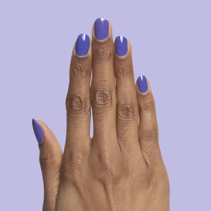 Hand displaying nails painted in glossy deep purple House of O&J polish against a soft lavender background for a stylish mani