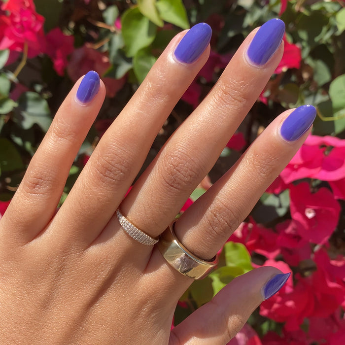 Hand with nails polished in glossy House of O&J deep purple polish wearing gold and silver rings outdoors