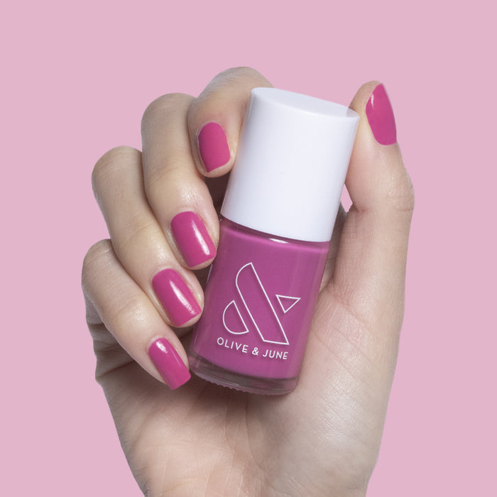 Hand holding a bottle of How Do You Spell Bougainvillea? nail polish with matching hot magenta mani against pink background