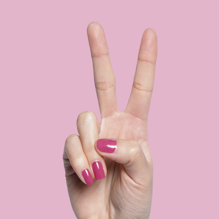 Hand showing nails with How Do You Spell Bougainvillea? polish in hot magenta against a soft pink backdrop