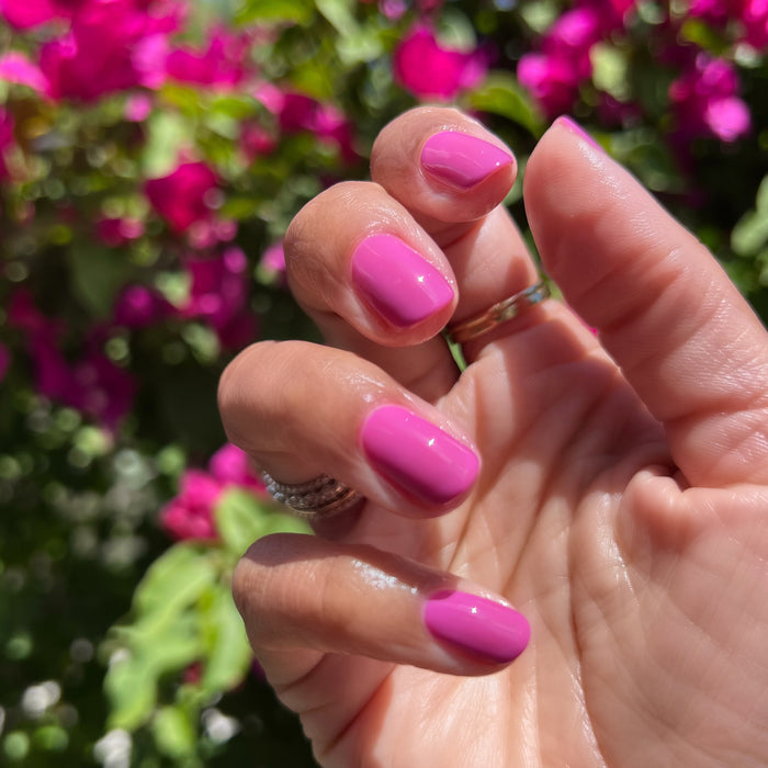 Hand with nails painted in vibrant hot magenta using How Do You Spell Bougainvillea? quick dry polish outdoors