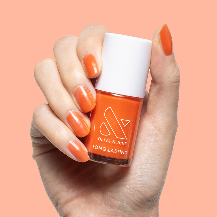 Hand holding Olive and June I’ll Take Another Spritz nail polish bottle with orange iridescent gel mani on nails
