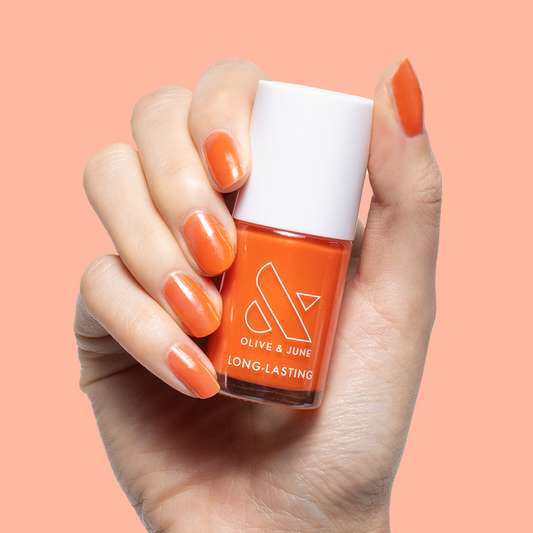 Hand holding Olive and June I’ll Take Another Spritz nail polish bottle with orange iridescent gel mani on nails