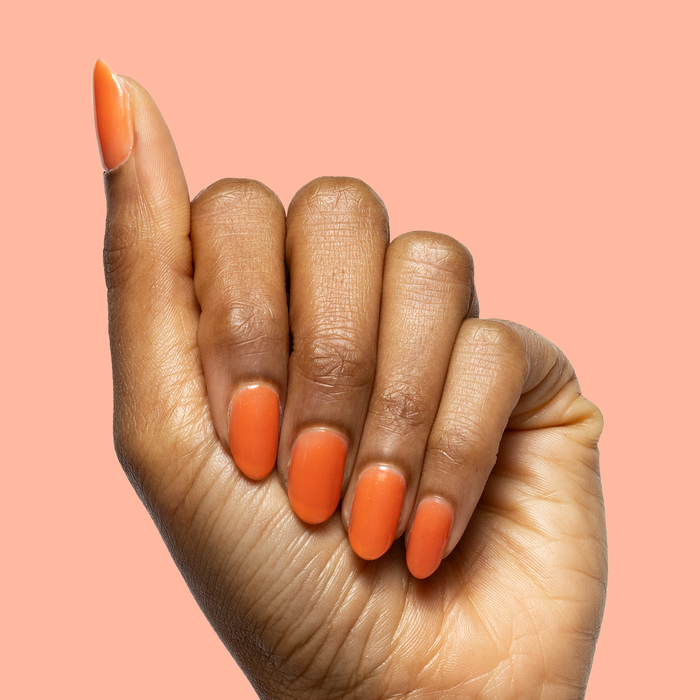 Hand with smooth nails painted in I’ll Take Another Spritz showing a sheer red-orange iridescent mani