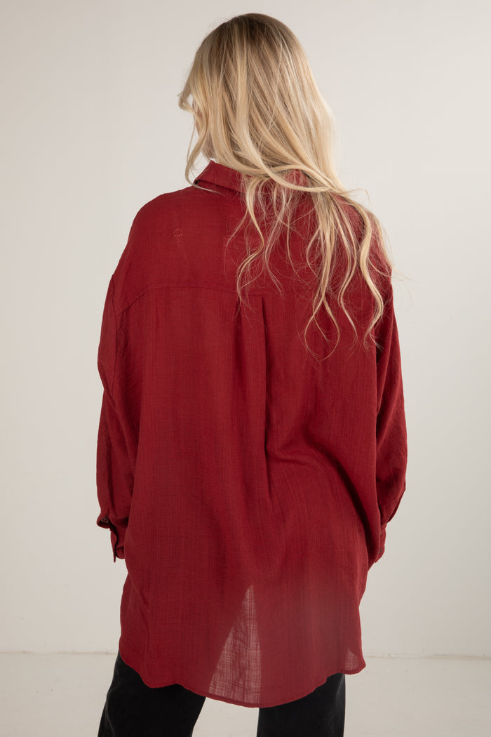 Person wearing a red shirt with long sleeves and a high collar, standing against a plain background.