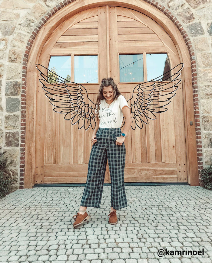 girl standing in front of large wooden door with black line drawing of angel wings behind her