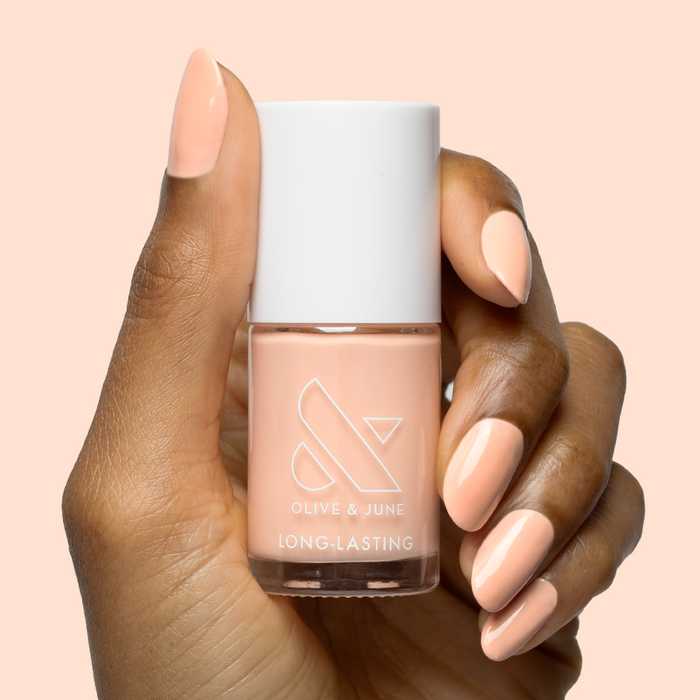 Hand with smooth nails painted in soft pastel melon shade It’s Serving Melon Cocktails nail polish by Olive and June