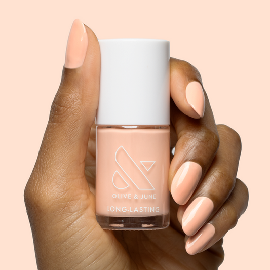 Hand with smooth nails painted in soft pastel melon shade It’s Serving Melon Cocktails nail polish by Olive and June