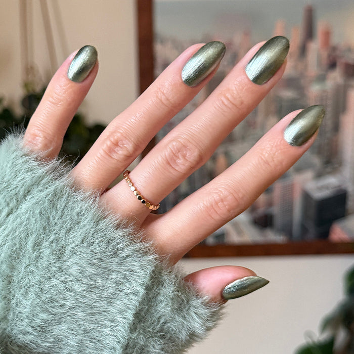 Hand with cool green metallic nails using Jade Velvet magnetic polish paired with cozy fuzzy sweater sleeve for manicure look