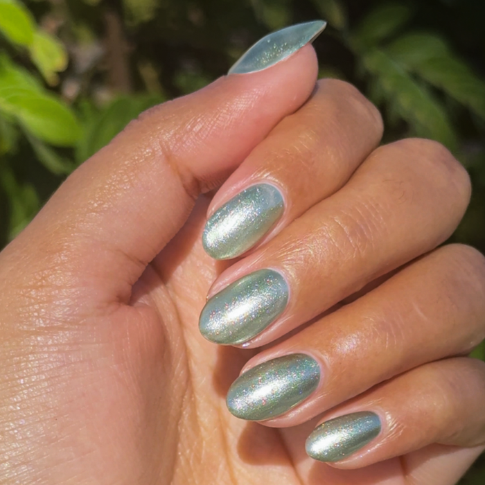 Hand with nails painted in Jade Velvet showing shimmering green magnetic polish in natural light outdoors