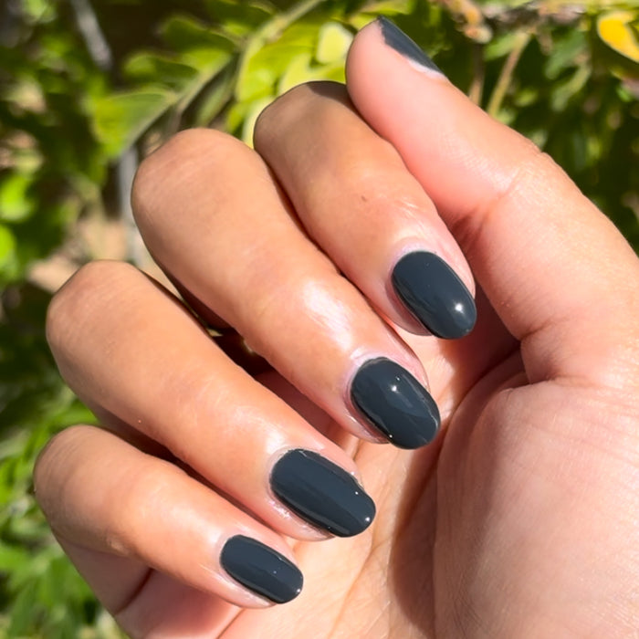 Hand with smooth deep charcoal gray nails painted in Last Minute Shopping gel polish by Olive and June for neat mani
