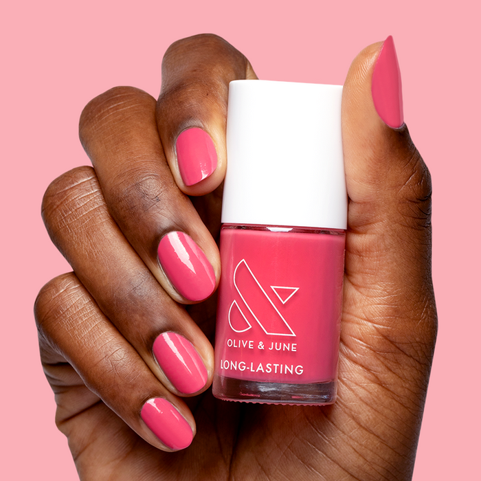 Hand holding bottle of Love All nail polish with matching bright hot pink manicure on nails
