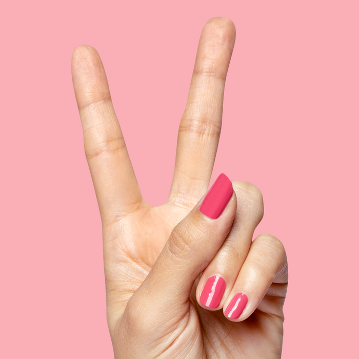Hand showing peace sign with nails polished in bright hot pink Love All for a vibrant at-home manicure look