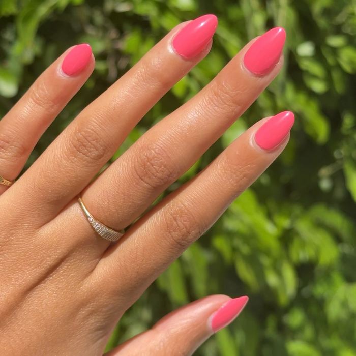 Hand with almond-shaped nails painted in bright pink gel polish for a lively Maine Character Energy manicure