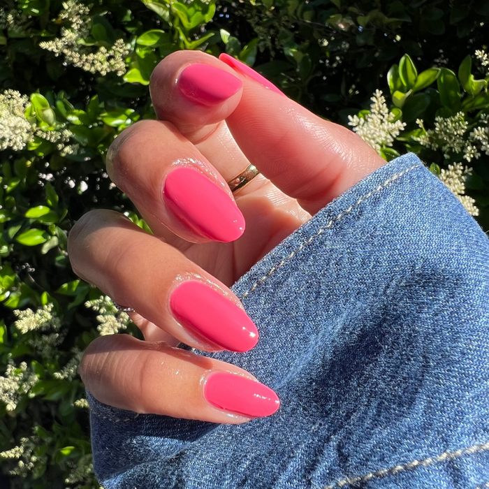 Hand with almond-shaped nails painted in glossy Maine Character Energy gel polish against green foliage background