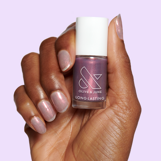 Hand holding Mermaid Hair nail polish bottle with sheer purple-pink-gold iridescent manicure on light purple background