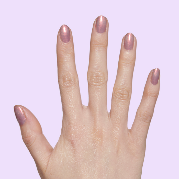 Hand with nails painted in shimmery purple-pink-gold polish Mermaid Hair showing iridescent manicure on light purple background