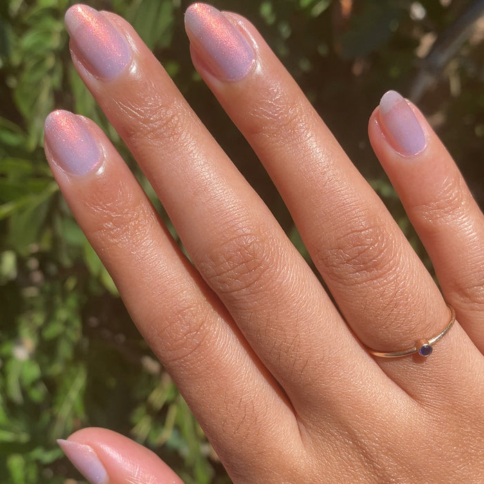 Fingernails painted with Mermaid Hair sheer iridescent polish reflecting pink, purple, and gold in natural sunlight outdoors