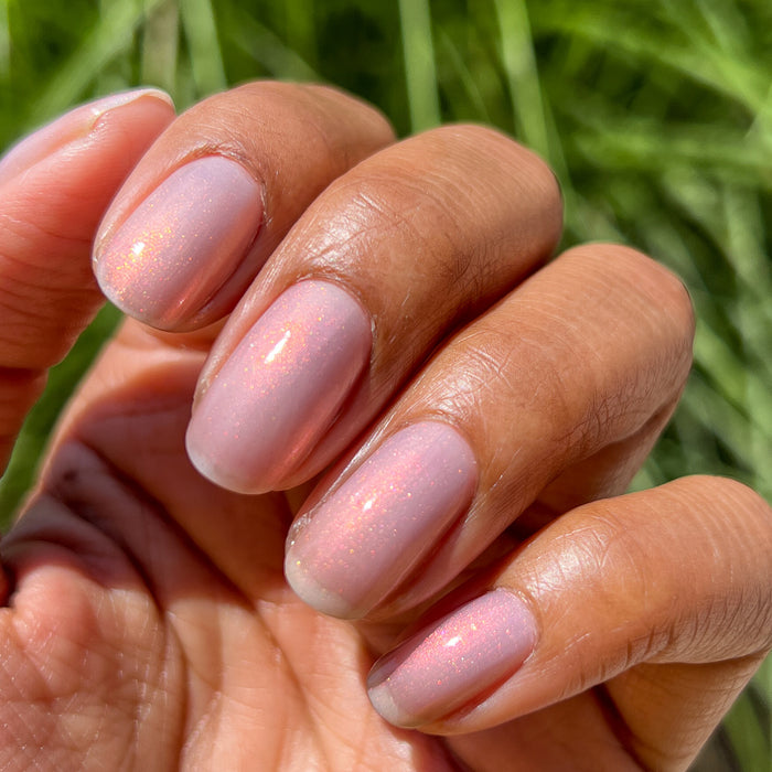 Hand with natural nails painted in sheer iridescent pink and gold shimmer polish Mermaid Hair in natural light outdoors