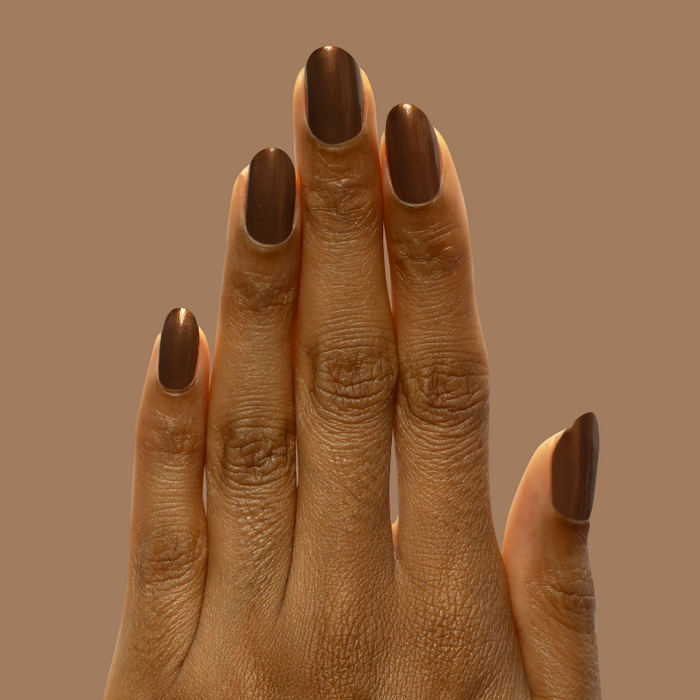 Hand with medium nails painted in Milk Chocolate gel polish with golden iridescent finish against brown background