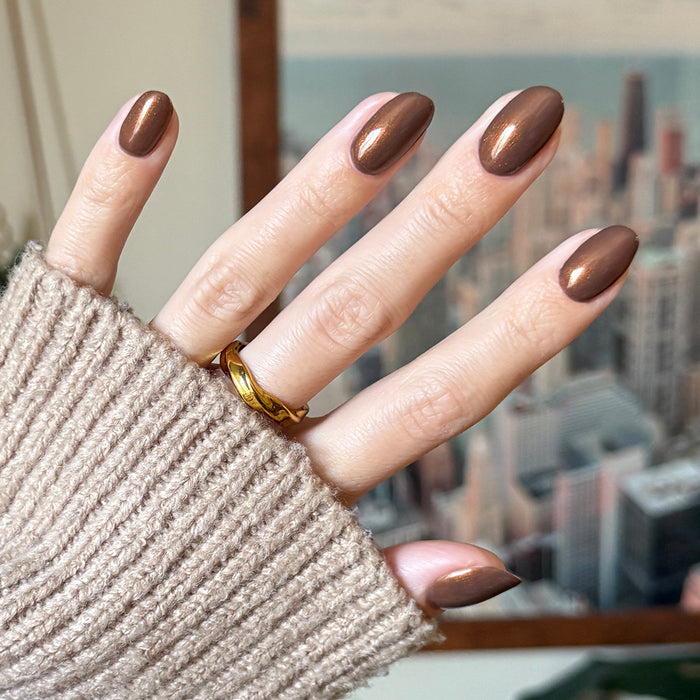 Hand with medium-length nails polished in Milk Chocolate gel polish showing smooth milky brown with subtle golden shine