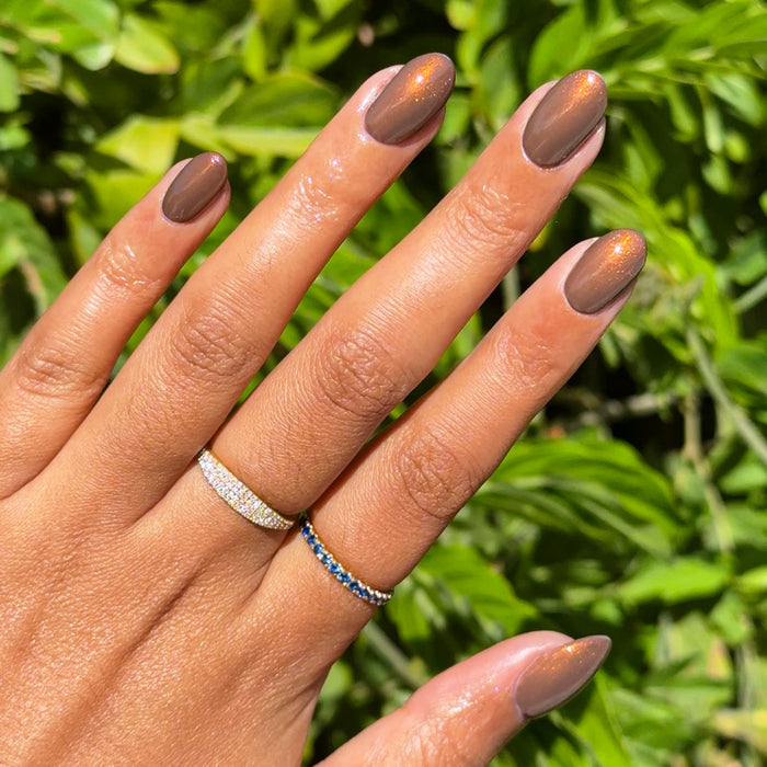 Hand with medium-length nails polished in Milk Chocolate showing creamy brown gel polish with subtle golden shimmer outdoors