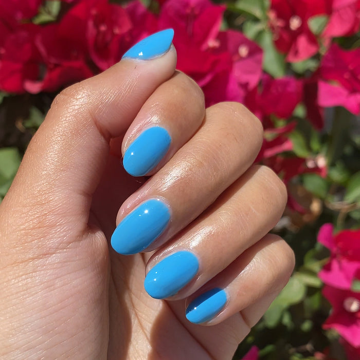 Hand with nails painted vibrant sky blue using Not a Cloud gel polish for a fresh at home manicure by Olive and June