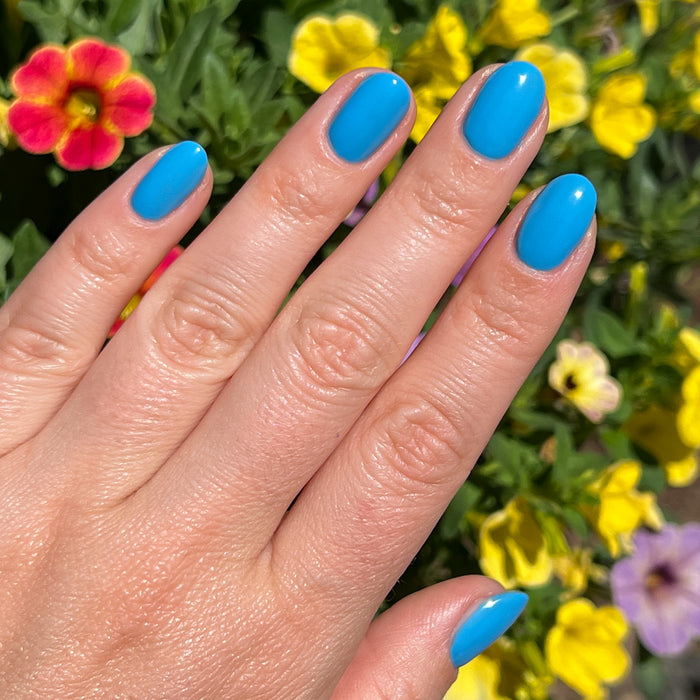 Hand with vibrant sky blue nails painted using Not a Cloud gel polish for a fresh at home manicure by Olive and June