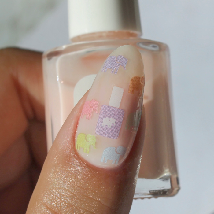 On Brand pastel elephant and polish bottle decals on a sheer nude nail, holding the bottle