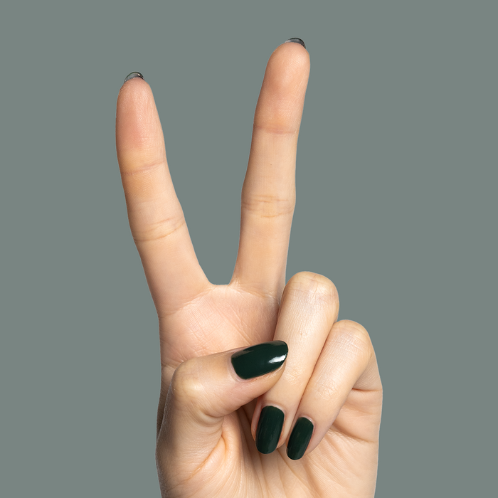Hand showing two fingers with nails painted moody dark emerald green One For You, Two For Me gel polish manicure