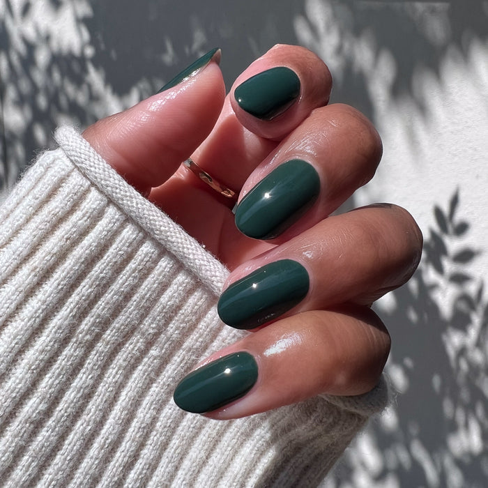 Hand with glossy nails painted in One For You, Two For Me gel polish showing dark emerald green mani