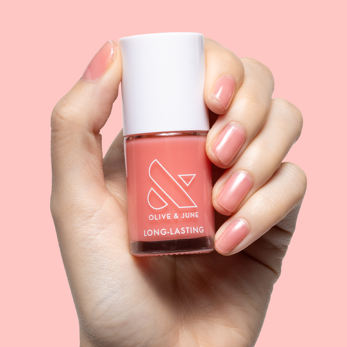 Hand holding Pink Pineapple Gloss nail polish bottle with matching warm peach pink glossy mani on nails