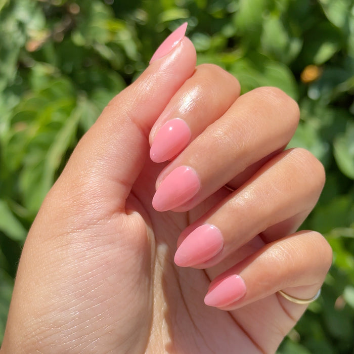 Hand with almond shaped nails painted in warm peach pink glossy Pink Pineapple Gloss nail polish outdoors