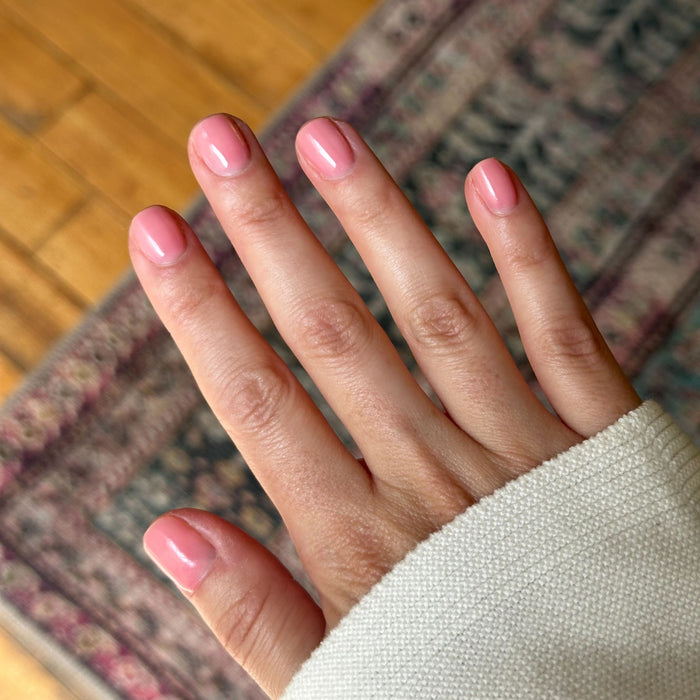 Hand with short rounded nails painted in sheer warm peach pink using Pink Pineapple Gloss nail polish indoors