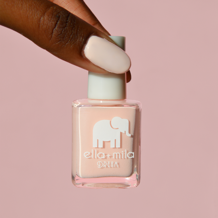 Pirouette warm nude pink nail polish on a deep skin tone, holding the bottle on a pink background