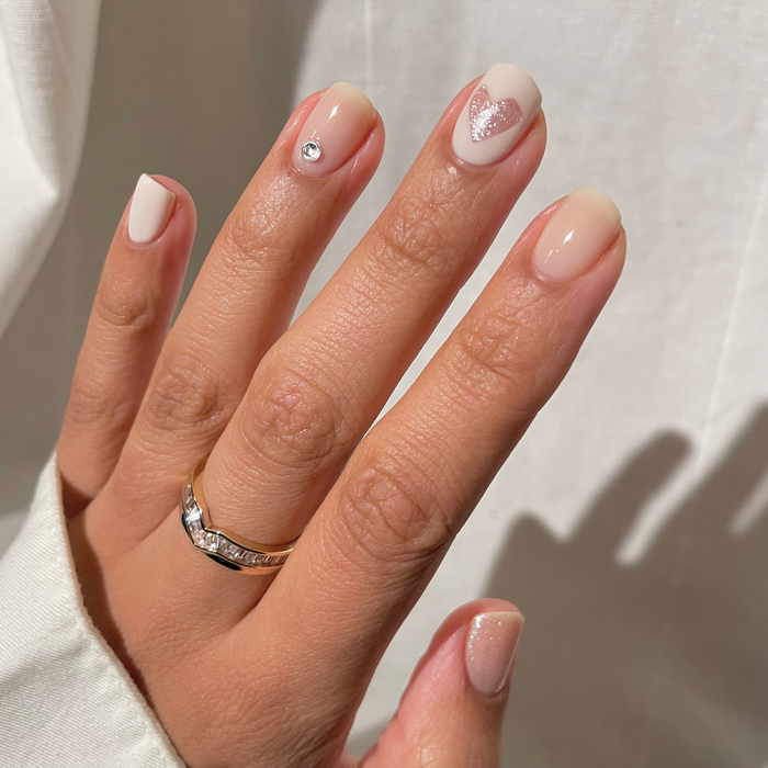 Pirouette nude pink manicure with tiny pearl and heart accents and a silver ring in sunlight