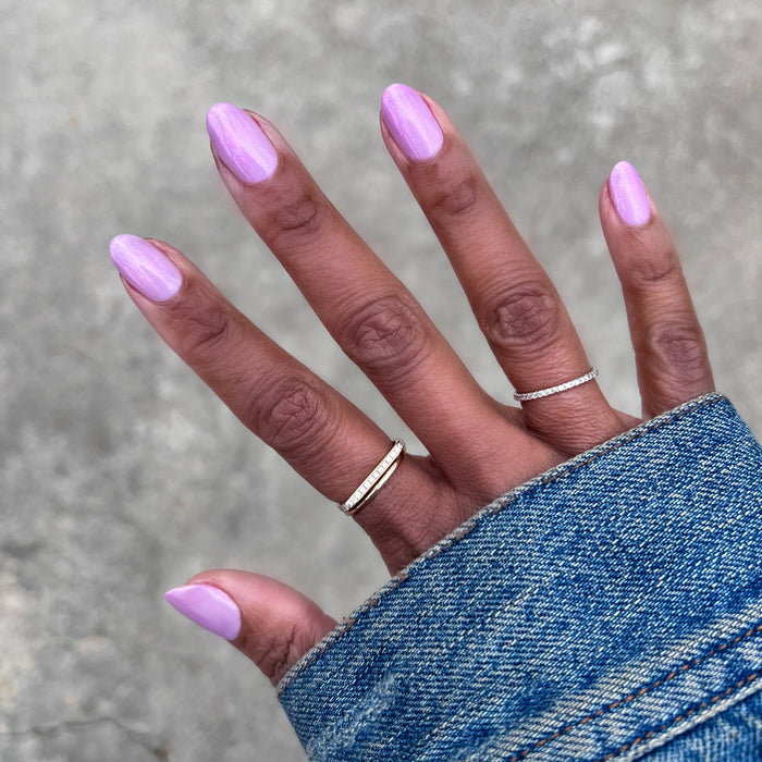 Purple Season manicure with soft purple nail polish on natural nails wearing silver rings and denim sleeve