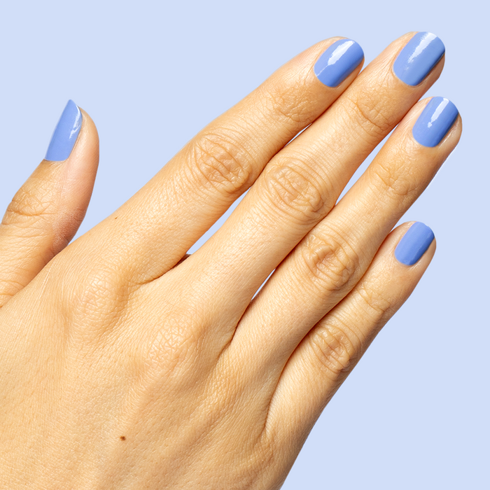 Hand with glossy nails painted in dusty ultramarine blue Rally Ready polish for a sporty at-home manicure look