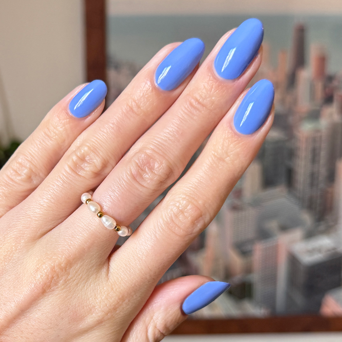 Hand with glossy nails painted in dusty ultramarine blue Rally Ready polish by Olive and June for a chic at-home manicure