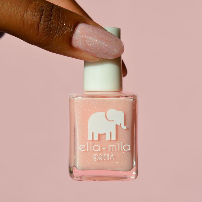 Relevé sheer pink shimmer nail polish on a deep skin tone, holding the bottle on a pink background