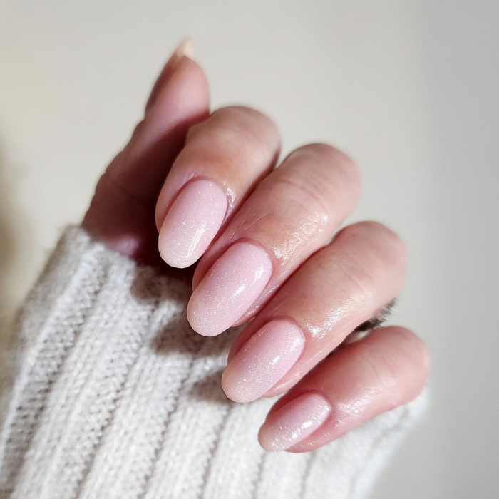 Relevé translucent pink shimmer nail polish manicure on a light skin tone with a white sweater