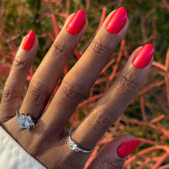 Hand showcasing Rodeo Queen - Press-On | Medium | Oval bright pinky-red shimmer false nails for an easy at-home manicure