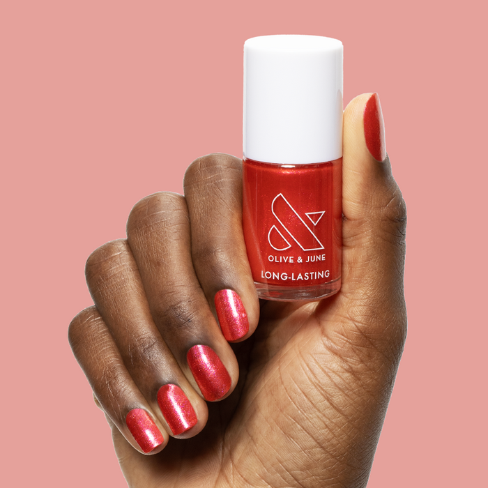 Hand holding Rodeo Queen bottle with bright pinky-red nail polish and silver shimmer for a long-lasting manicure