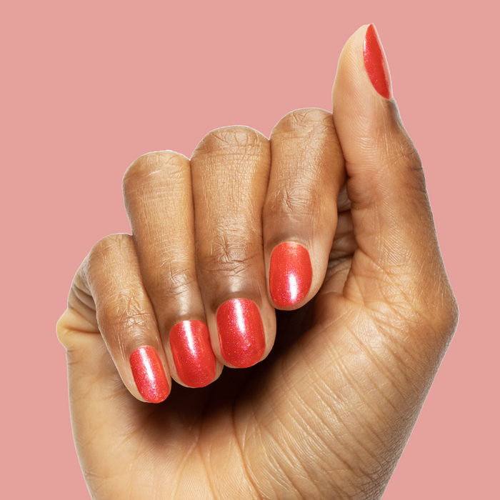 Hand with medium length nails painted bright pinky-red with silver shimmer using Rodeo Queen polish for a mani